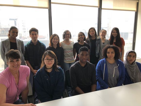 Twelve students gather with their clinical advisor. Five people are seated and the remaining are standing behind them.