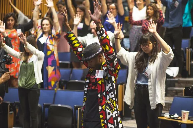 Participants of the symposium raise their hands above their hands.