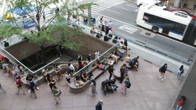 View from Hunter bridge looking down to the subway entrance. People sit on benches and walk by.