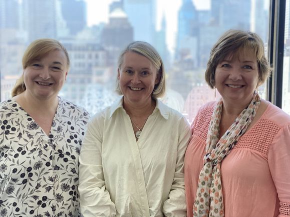 Gina Riley, Rebecca English and Julie Gorlewski smile in front of a large window.