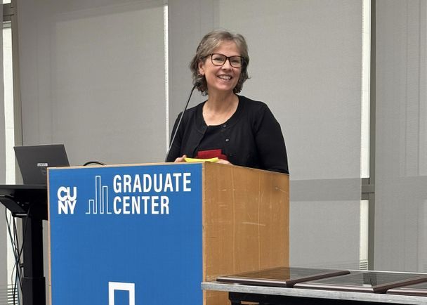 Rhonda Bondie speaking at the awards ceremony. The podium has a blue banner on it that says 